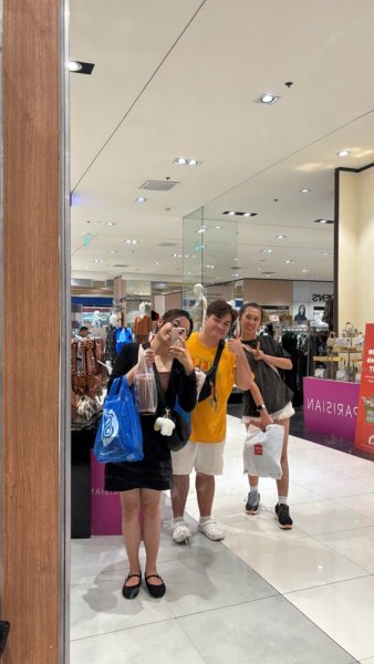 在百貨公司服飾區的鏡子前,三人提著購物袋自拍