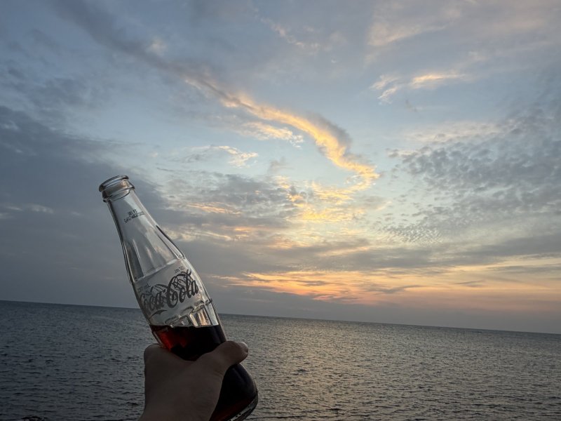 海邊夕陽下，手舉一瓶玻璃瓶可樂