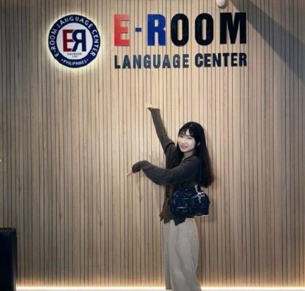 兩週遊學期間,學員在 e-Room 大廳的木條招牌牆前舉手比向學校招牌